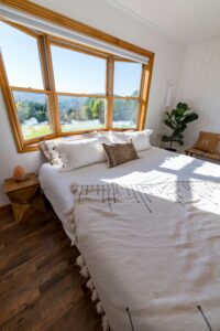Helles Schlafzimmer mit großem Fenster, weißer Bettwäsche und Tageslicht, Ordnung bringt Licht, Luft und Klarheit in den Raum 
